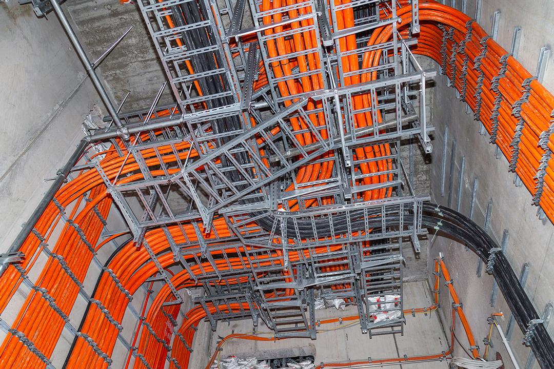 Installierte Kabelleitern mit dicken orangefarbenen und schwarzen Kabeln in einem Raum mit Betonwänden