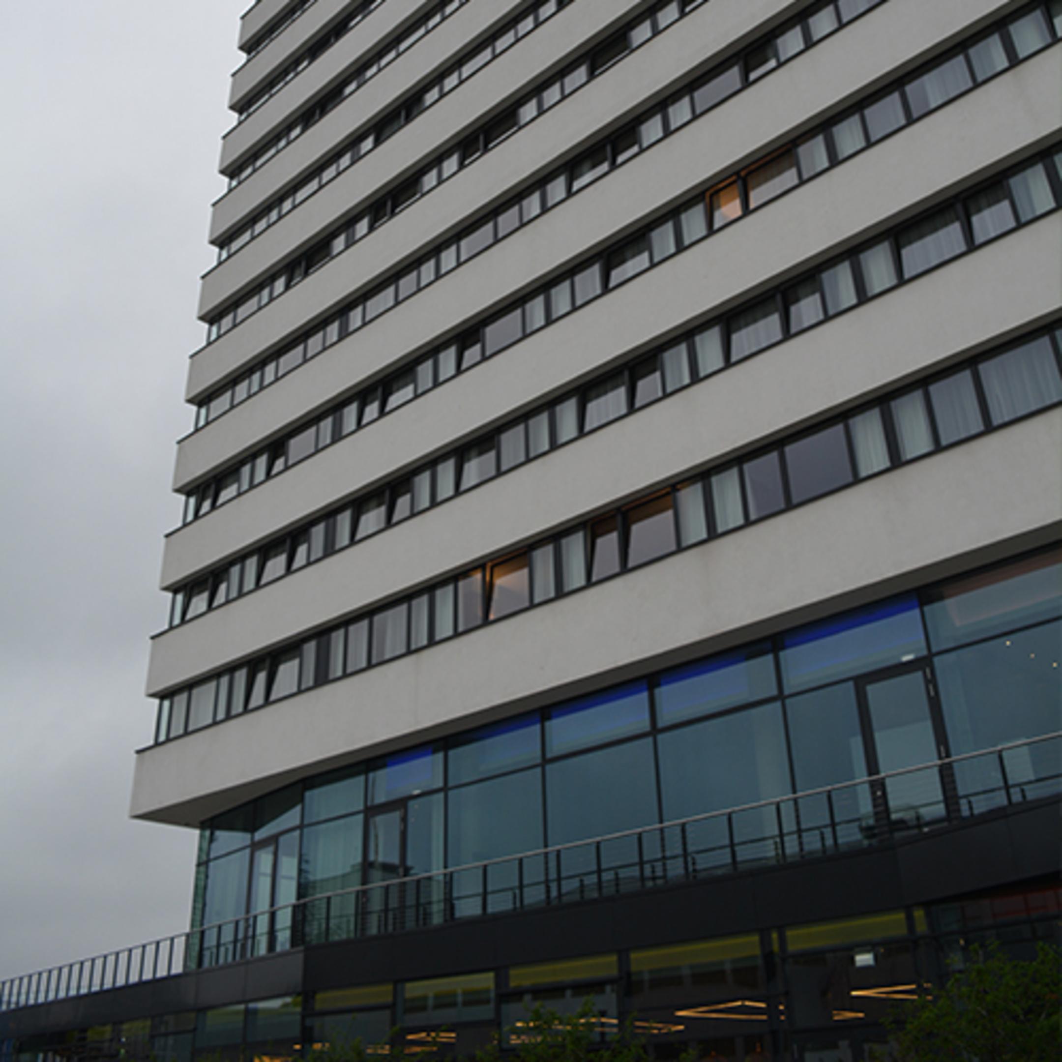Blick von unten auf ein mehrstöckiges Gebäude mit Fensterfront, bewölkter Himmel