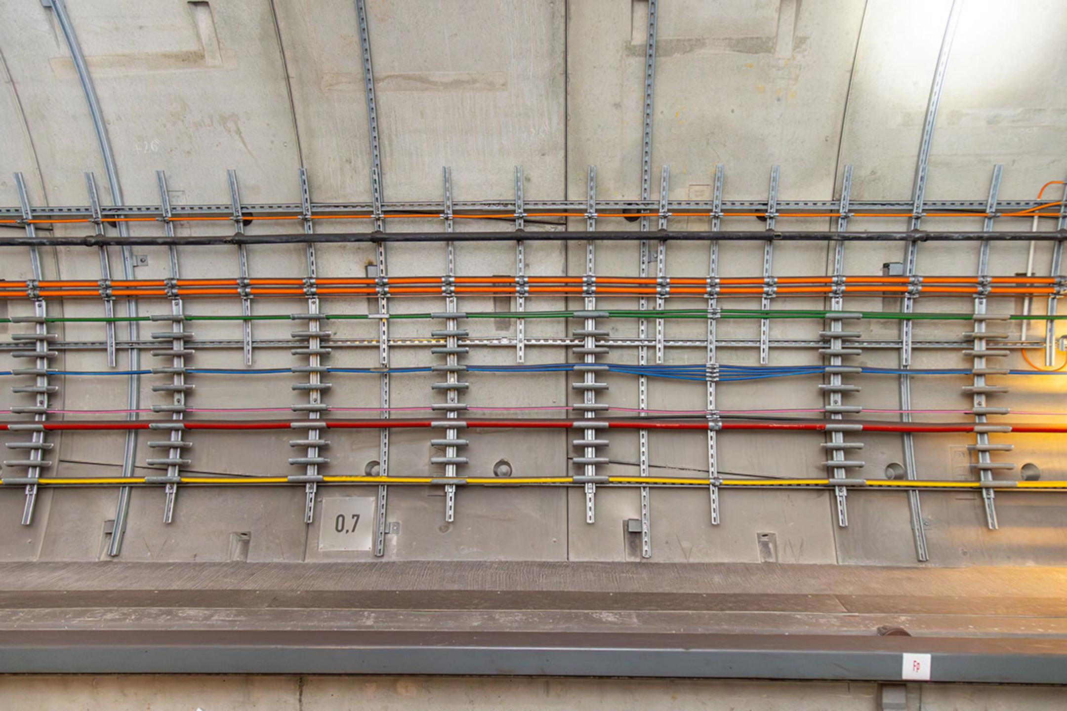 Farbcodierte Kabel befestigt an der Betonwand eines Bahntunnels, sauber organisiert und sicher befestigt