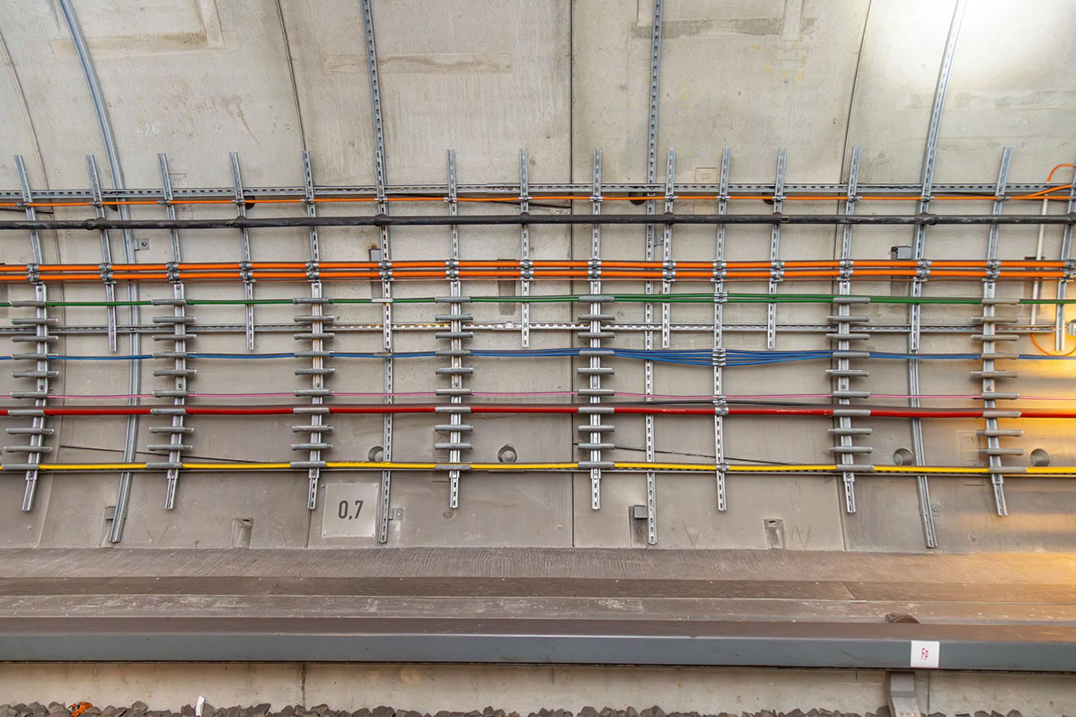 Farbcodierte Kabel befestigt an der Betonwand eines Bahntunnels, sauber organisiert und sicher befestigt