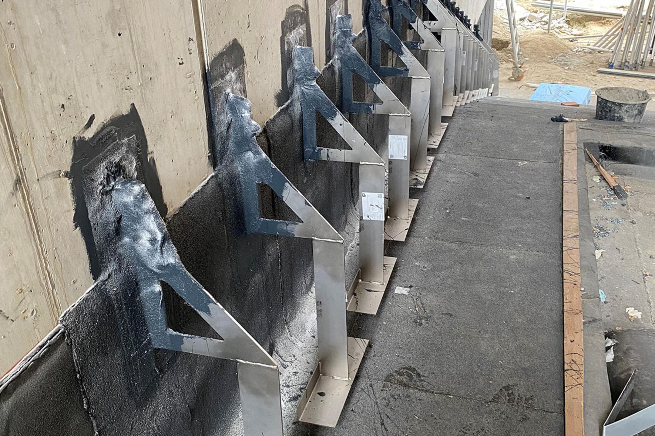 Reihe aus Verblenderkonsolen an einer Wand auf einer Baustelle mit Baumaterialien im Hintergrund