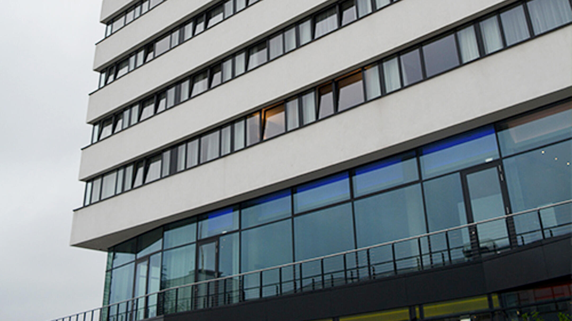 Blick von unten auf ein mehrstöckiges Gebäude mit Fensterfront, bewölkter Himmel