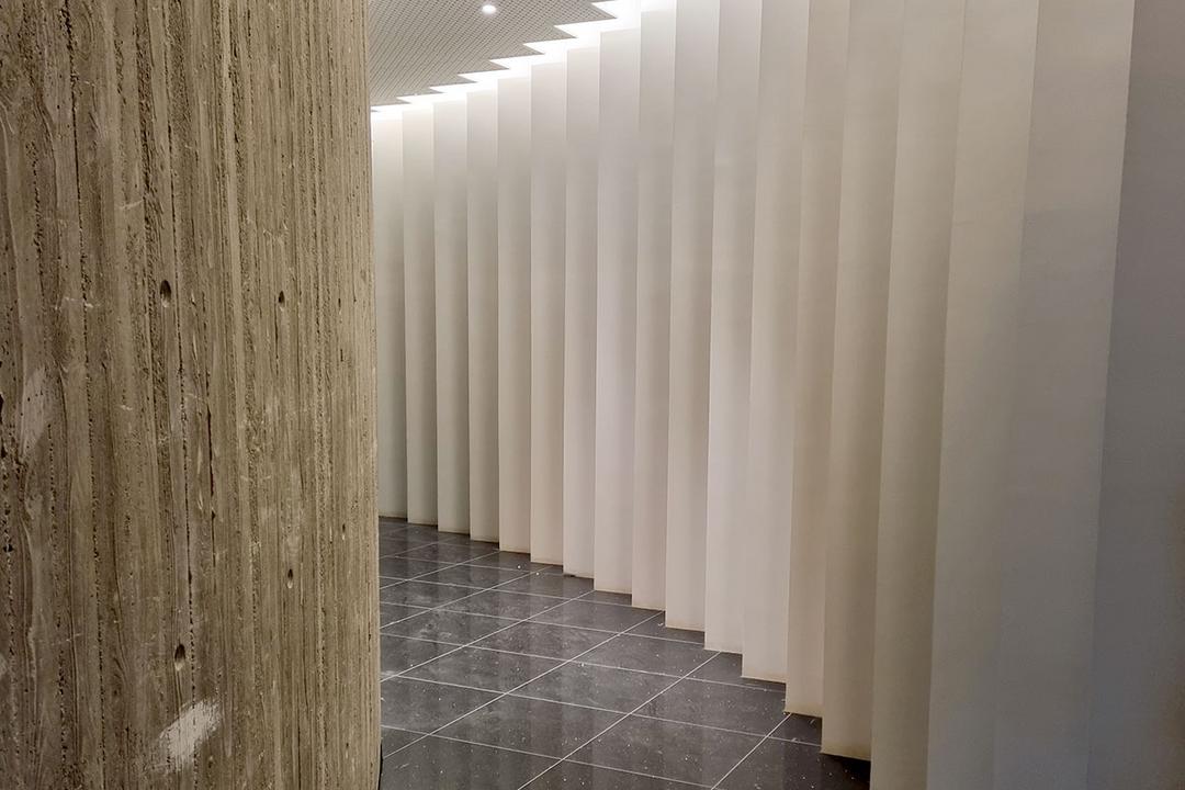 Gebogener Sichtbeton links, rechts weiße vertikale Lamellen, glänzender schwarzer Fliesenboden darunter