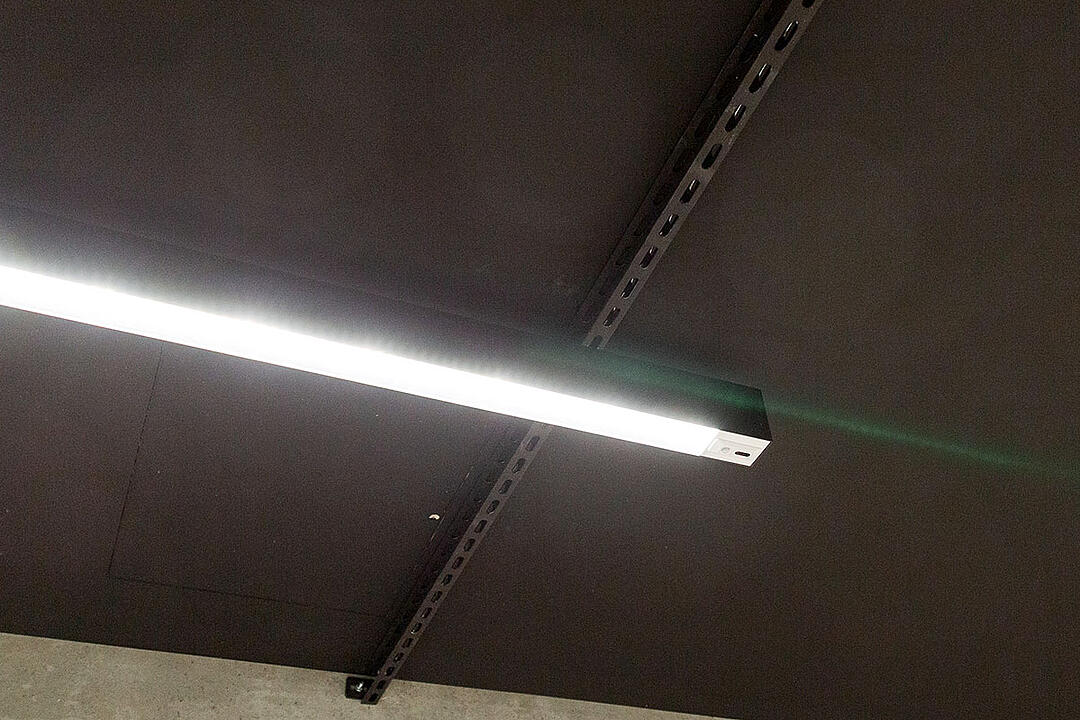 Leuchtende, längliche Deckenlampe an schwarzer Decke mit sichtbaren Metallträgern