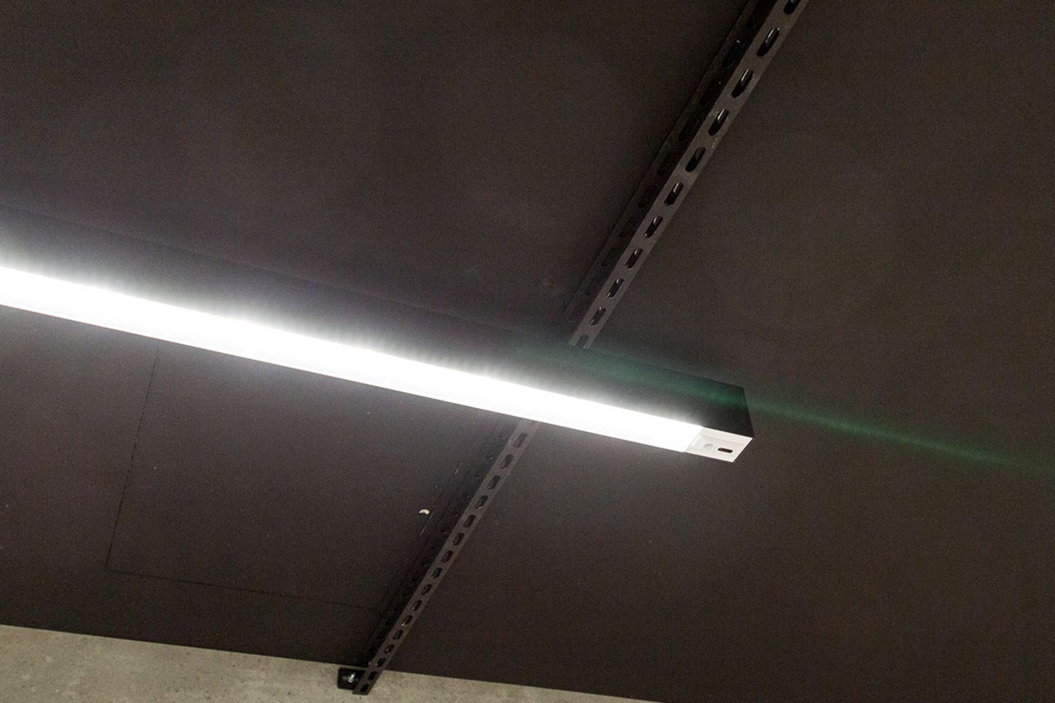 Leuchtende, längliche Deckenlampe an schwarzer Decke mit sichtbaren Metallträgern