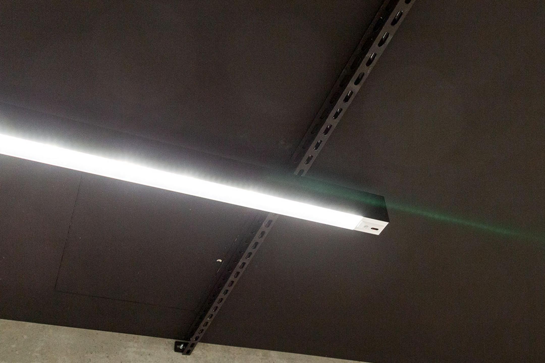 Leuchtende, längliche Deckenlampe an schwarzer Decke mit sichtbaren Metallträgern