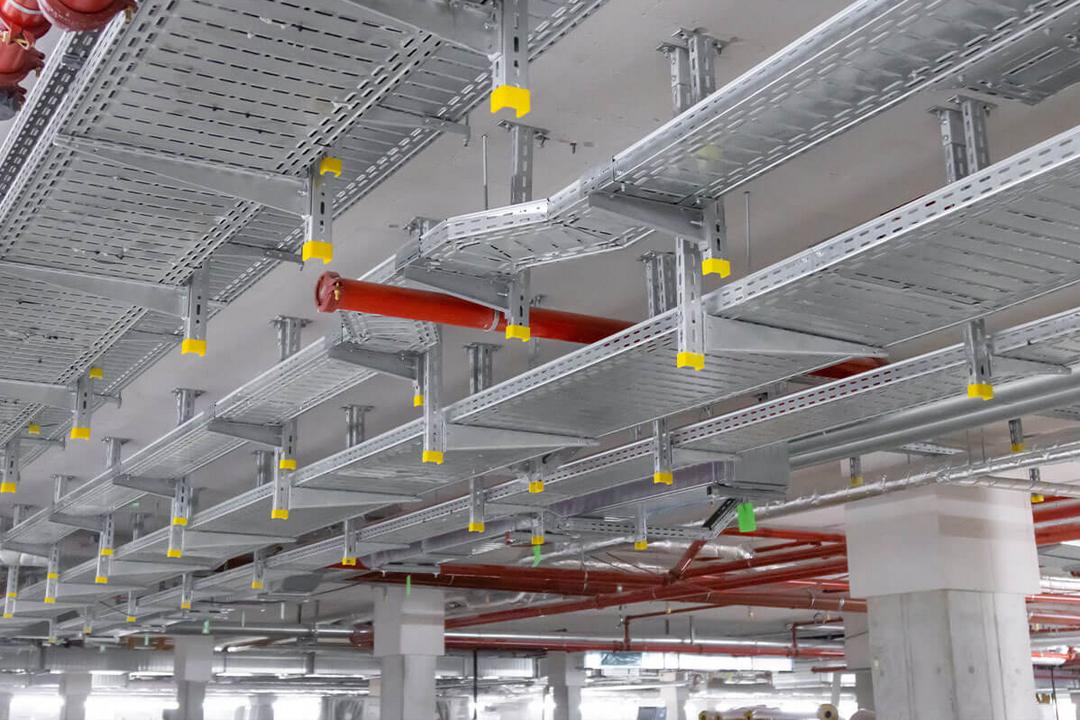 Mithilfe von Konsolen sind Kabelrinnen an der Decke befestigt, dazwischen verlaufen rote Rohrleitungen