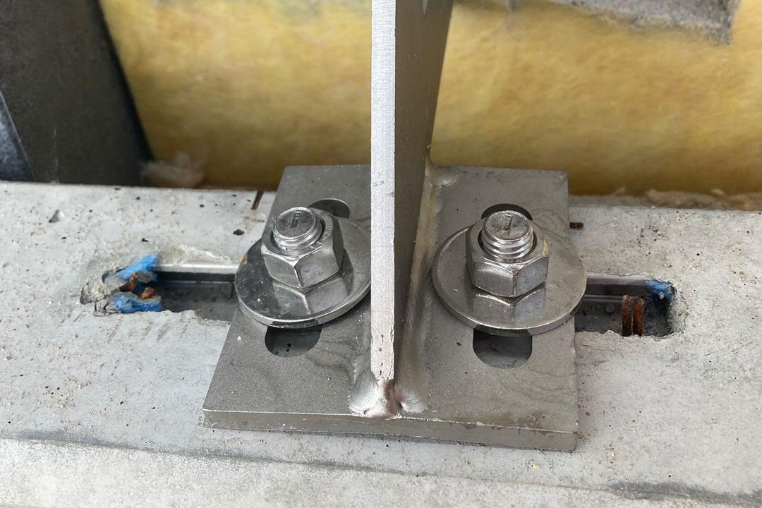 Nahaufnahme einer Verblenderkonsole mit zwei Schrauben, Muttern und Unterlegscheiben auf einem Betonuntergrund
