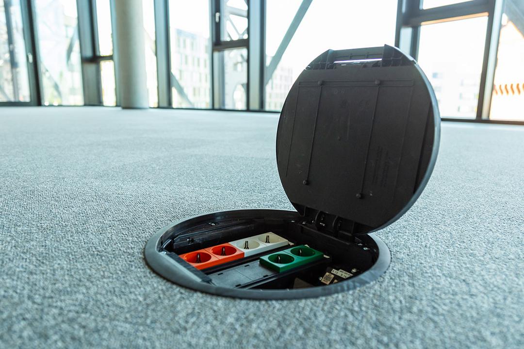 Geöffnete Einbaueinheit im Teppichboden in einem modernen Büro mit Panoramafenstern