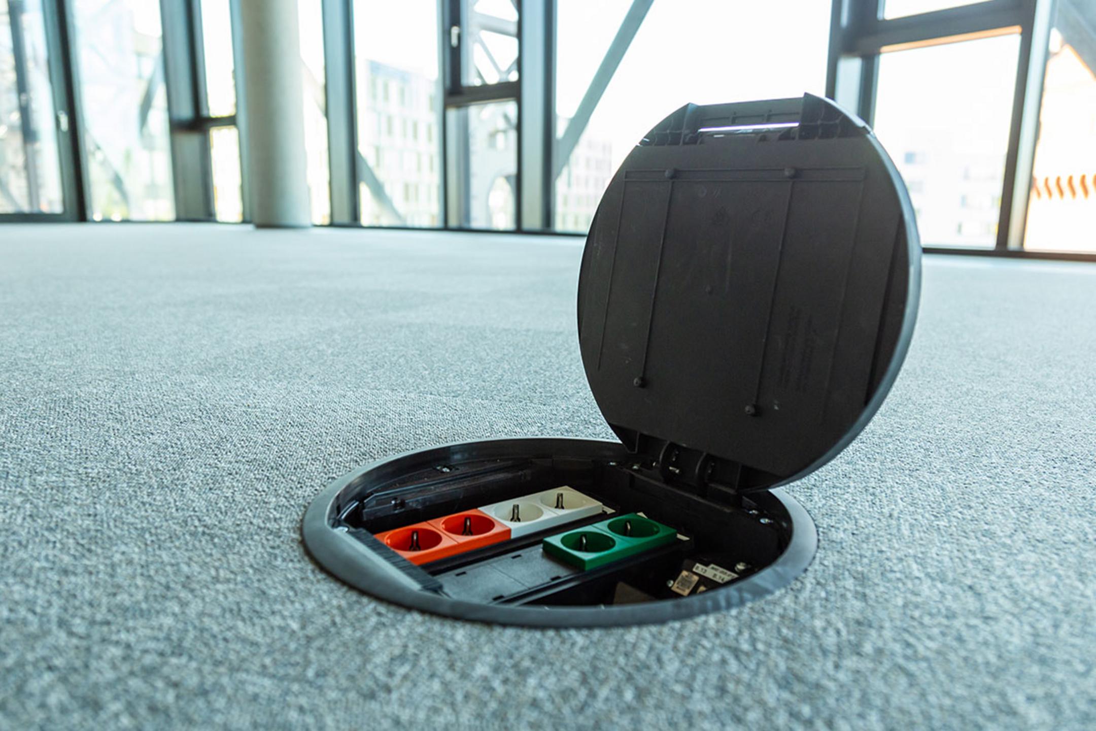 Geöffnete Einbaueinheit im Teppichboden in einem modernen Büro mit Panoramafenstern