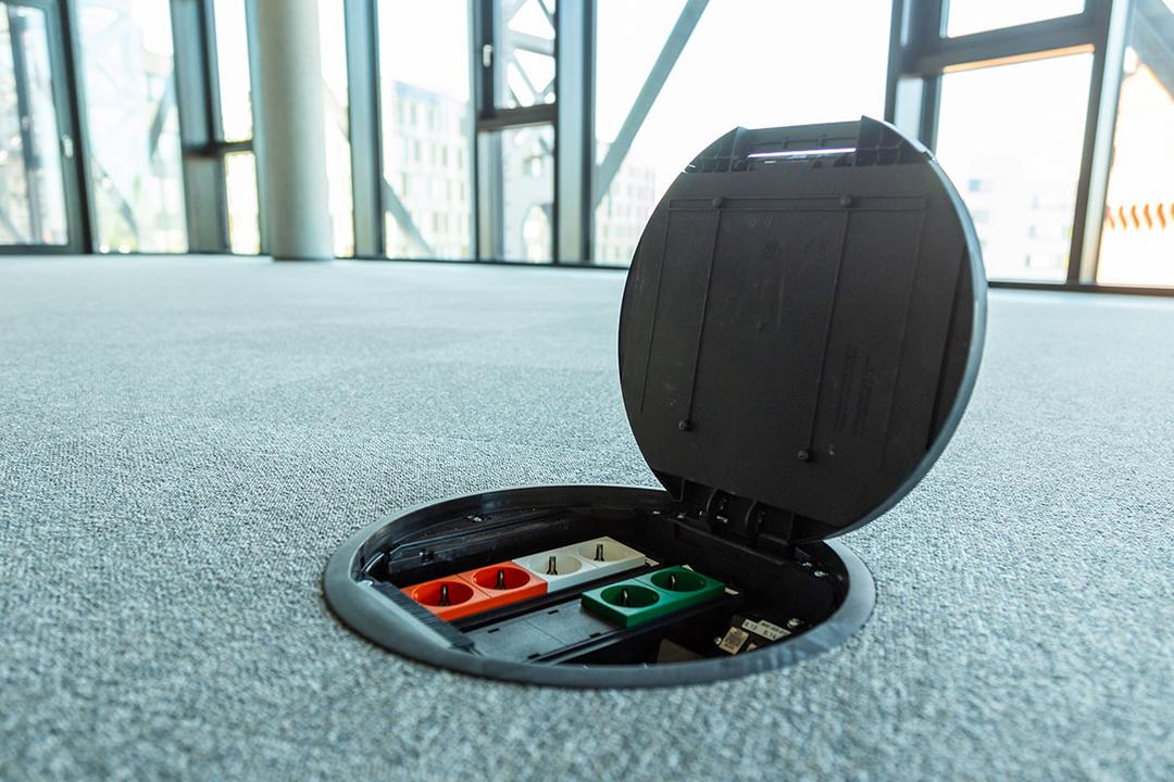 Geöffnete Einbaueinheit im Teppichboden in einem modernen Büro mit Panoramafenstern