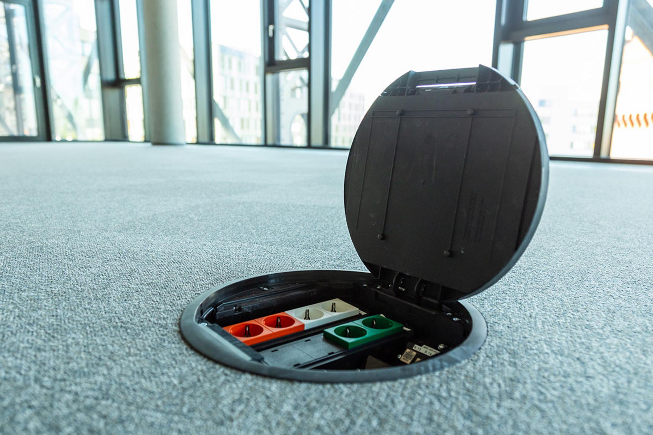 Geöffnete Einbaueinheit im Teppichboden in einem modernen Büro mit Panoramafenstern