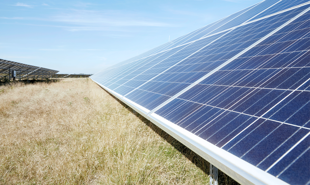 Nahaufnahme von Photovoltaikmodulen auf einer Freifläche mit trockener Wiese unter blauem Himmel bei Sonnenschein.