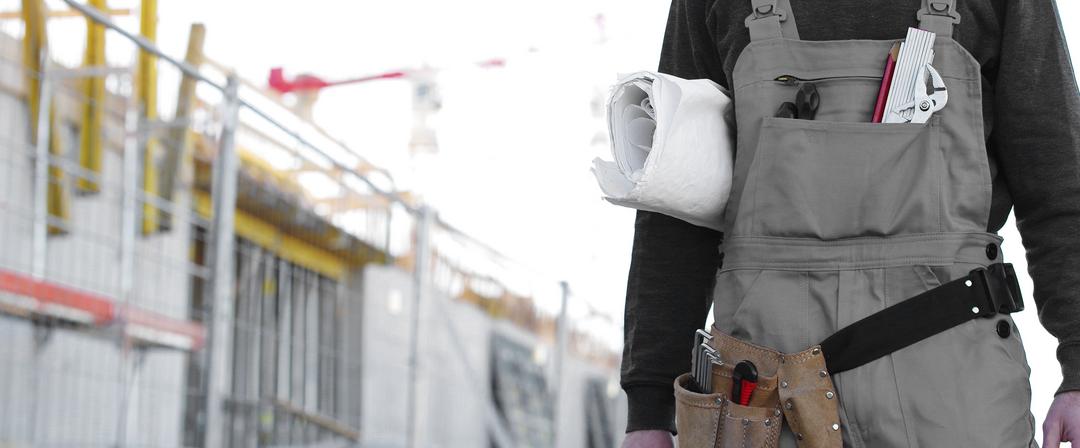 Mensch im Anschnitt mit zusammengerolltem Bauplan unter dem Arm auf einer Baustelle