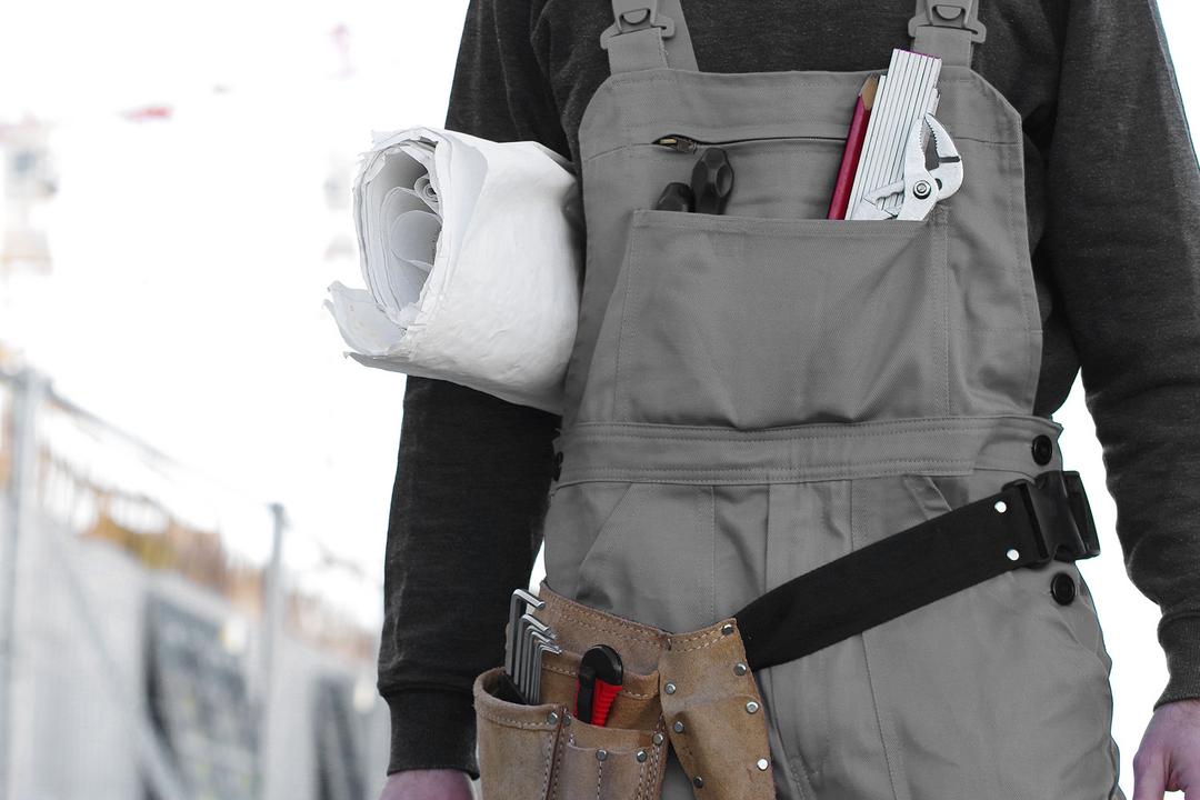 Mensch im Anschnitt mit zusammengerolltem Bauplan unter dem Arm auf einer Baustelle