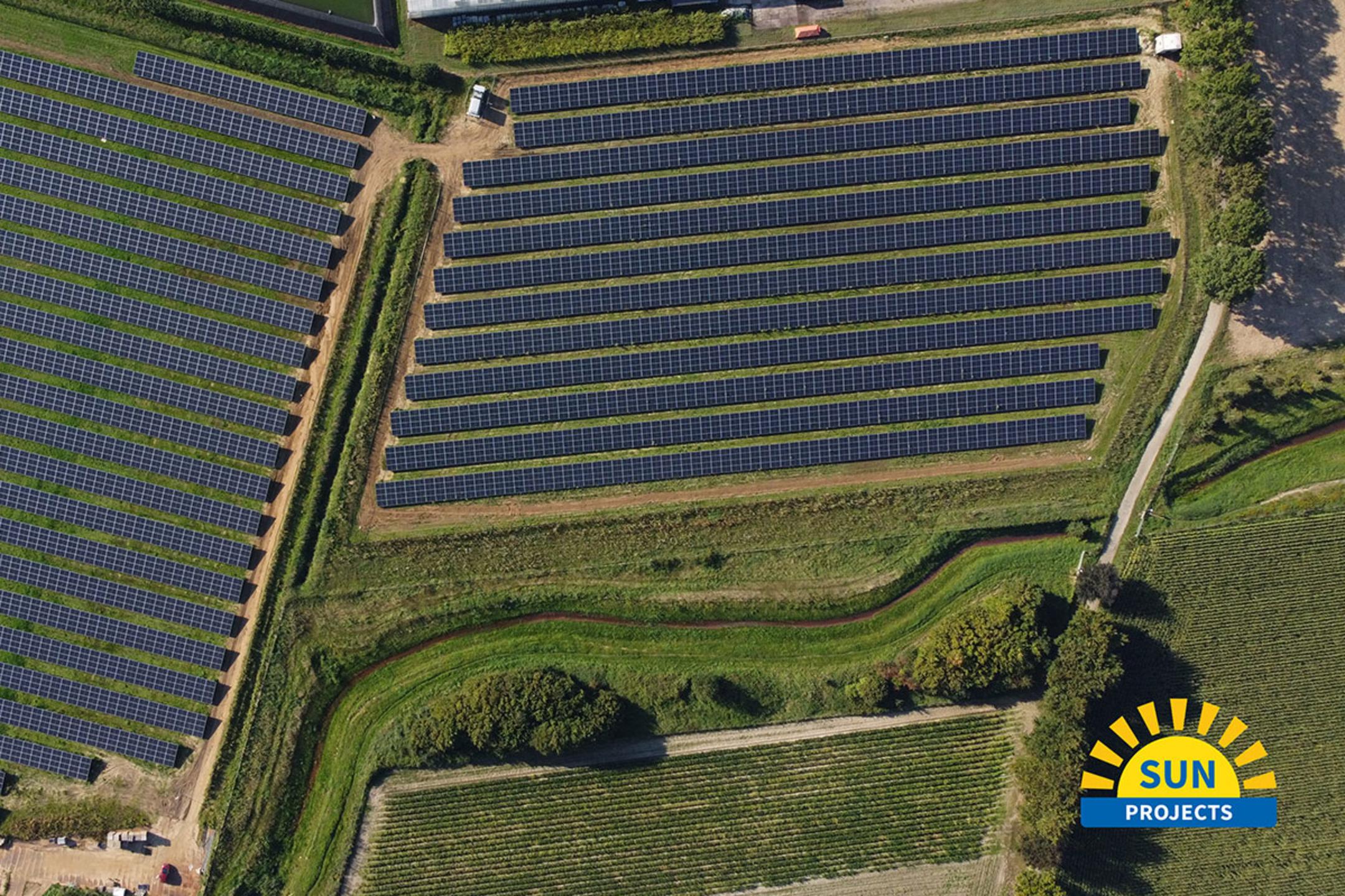 Luftaufnahme einer landwirtschaftlichen Fläche mit Solarpanelen und Gewächshäusern im Anschnitt