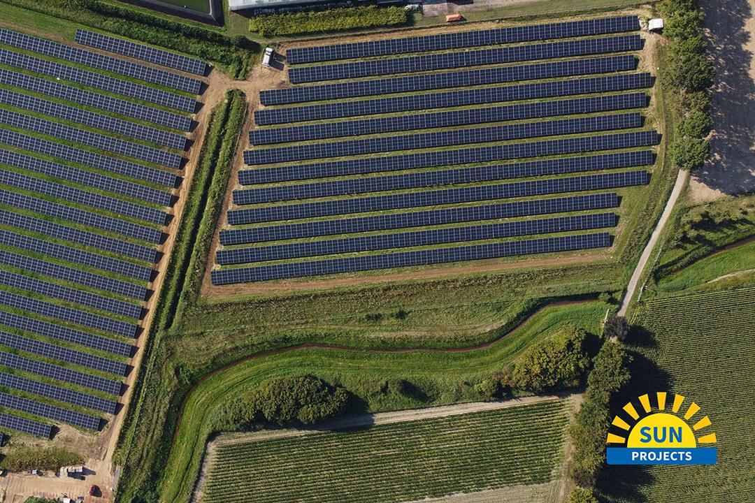 Luftaufnahme einer landwirtschaftlichen Fläche mit Solarpanelen und Gewächshäusern im Anschnitt