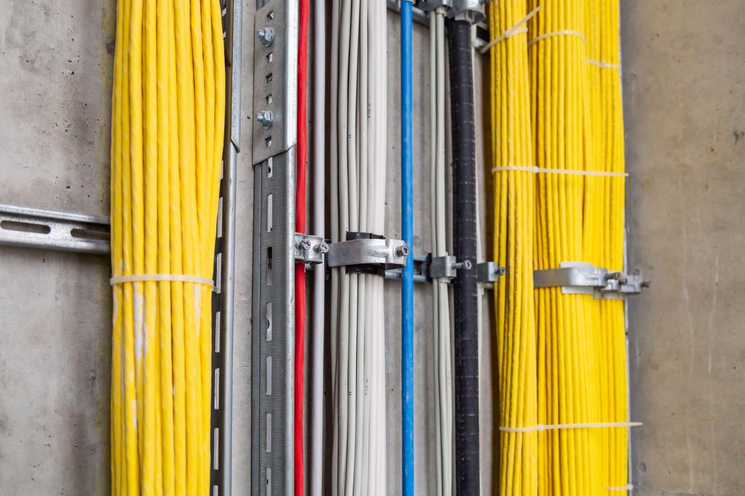 Saubere Elektroinstallation mit farbcodierten Kabeln in stabilen Metalltrassen an der Wand montiert.