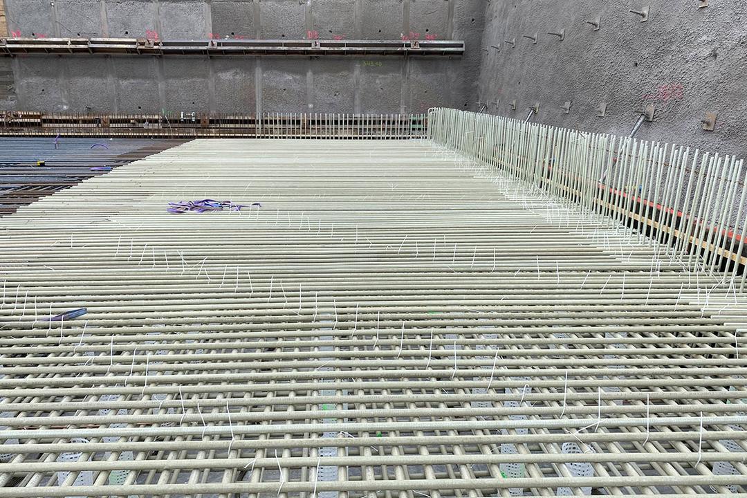 Detailaufnahme von verlegten Glasfaserkunststoffbewehrungsstäben mit Abstandshaltern auf einer Bodenplatte in einer Baugrube