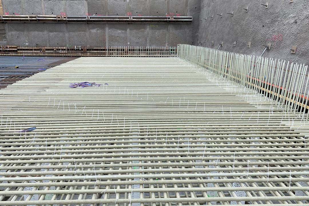 Detailaufnahme von verlegten Glasfaserkunststoffbewehrungsstäben mit Abstandshaltern auf einer Bodenplatte in einer Baugrube