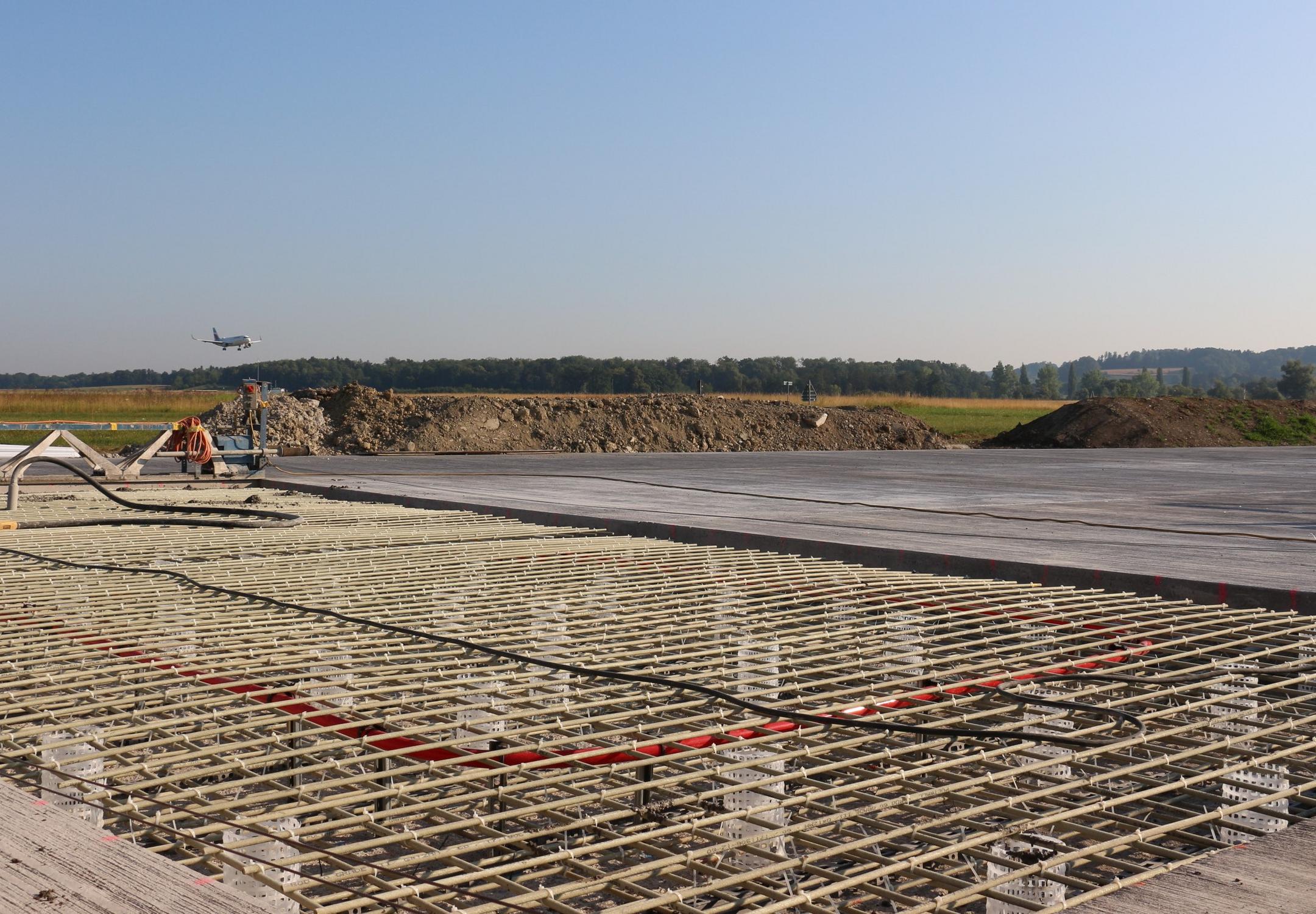 Blick auf die Baustelle, im Hintergrund grüne Felder und Wälder sowie blauer Himmel.
