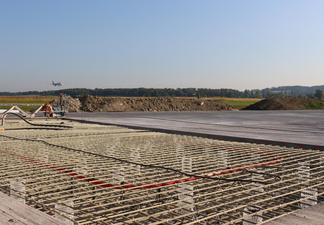 Blick auf die Baustelle, im Hintergrund grüne Felder und Wälder sowie blauer Himmel.