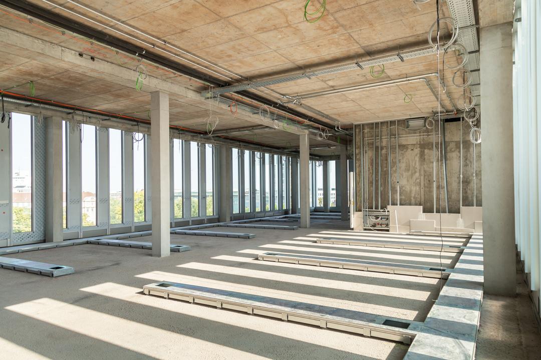 Rohbau mit bodentiefen Fenstern und Kabeltrassen zur Leitungsverlegung an der Decke, auf dem Boden befindet sich ein Bodenkanalsystem