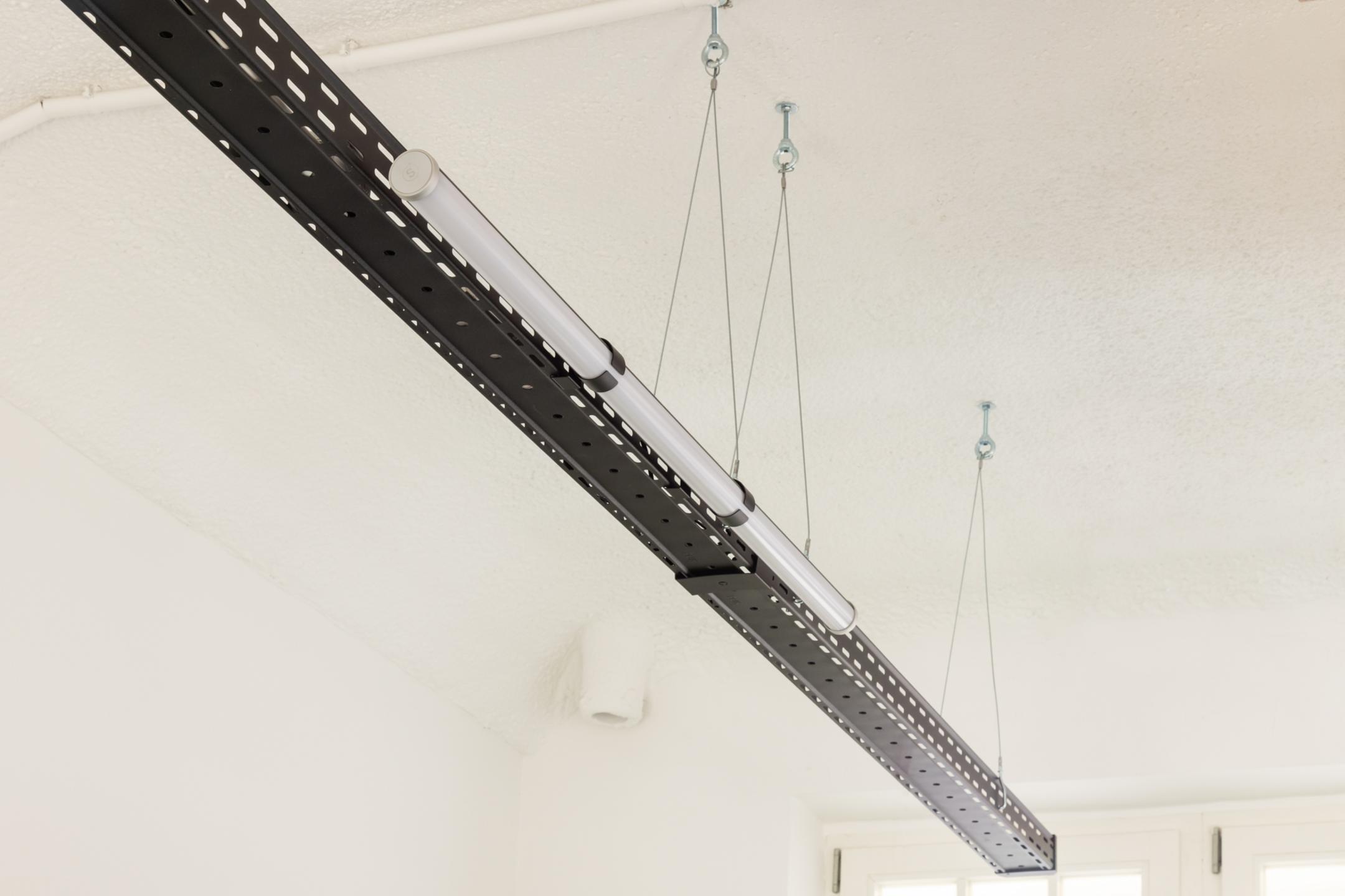 Eine schwarze Kabelrinne hängt von der Decke, daran ist eine schmale runde Leuchte befestigt.