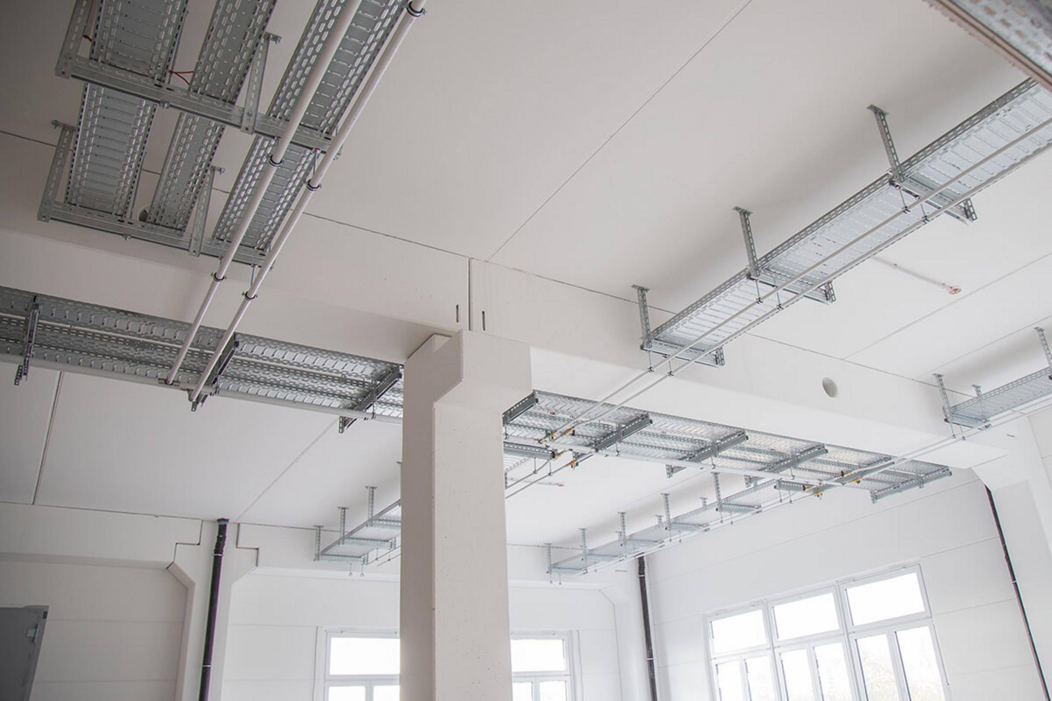 Die Kabeltragsysteme an der Decke des Erweiterungsbaus aus einer anderen Perspektive, in einem lichtdurchfluteten Raum..