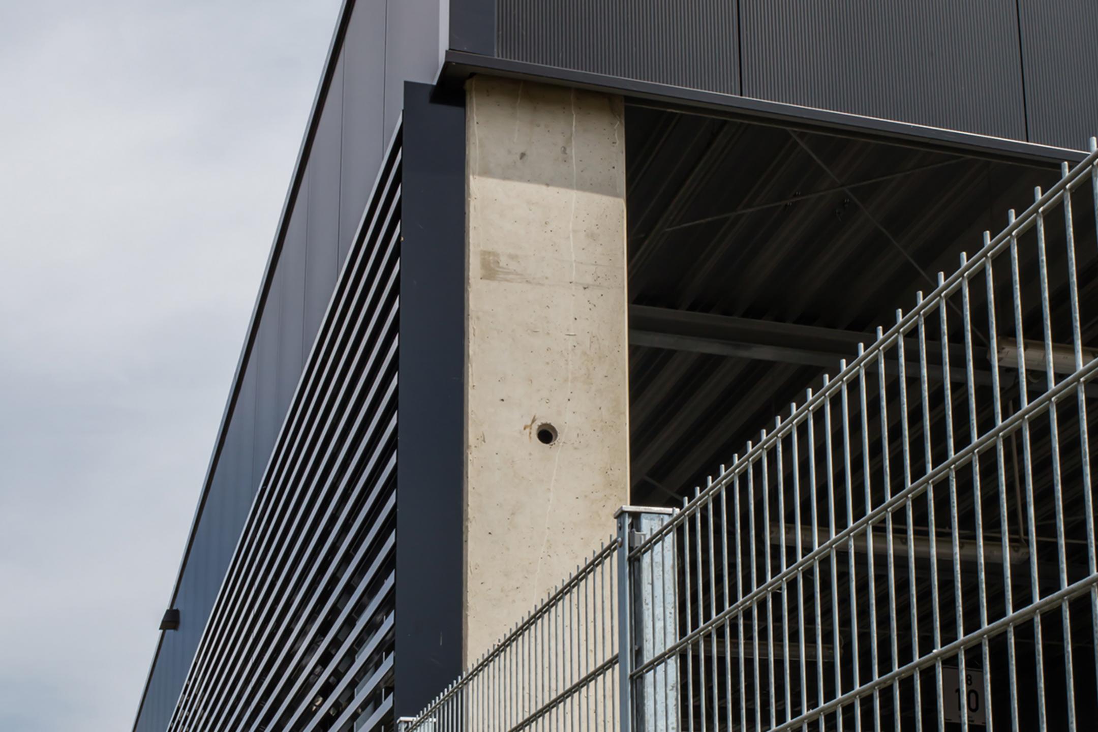 Der Firmenneubau aus der Nähe betrachtet, im Vordergrund ein Gitterzaun aus Metall.