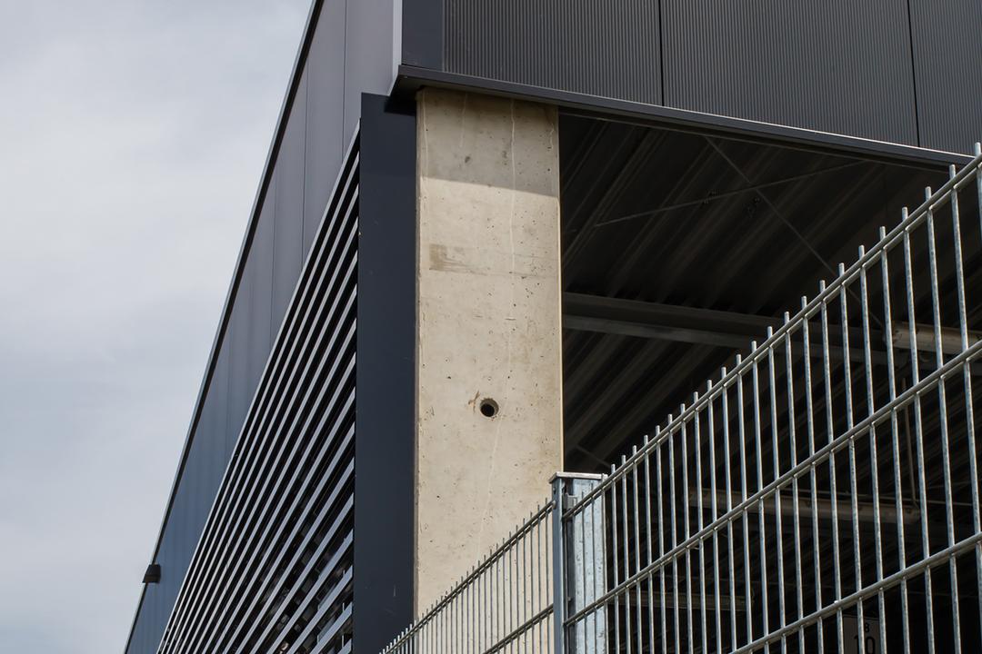 Der Firmenneubau aus der Nähe betrachtet, im Vordergrund ein Gitterzaun aus Metall.