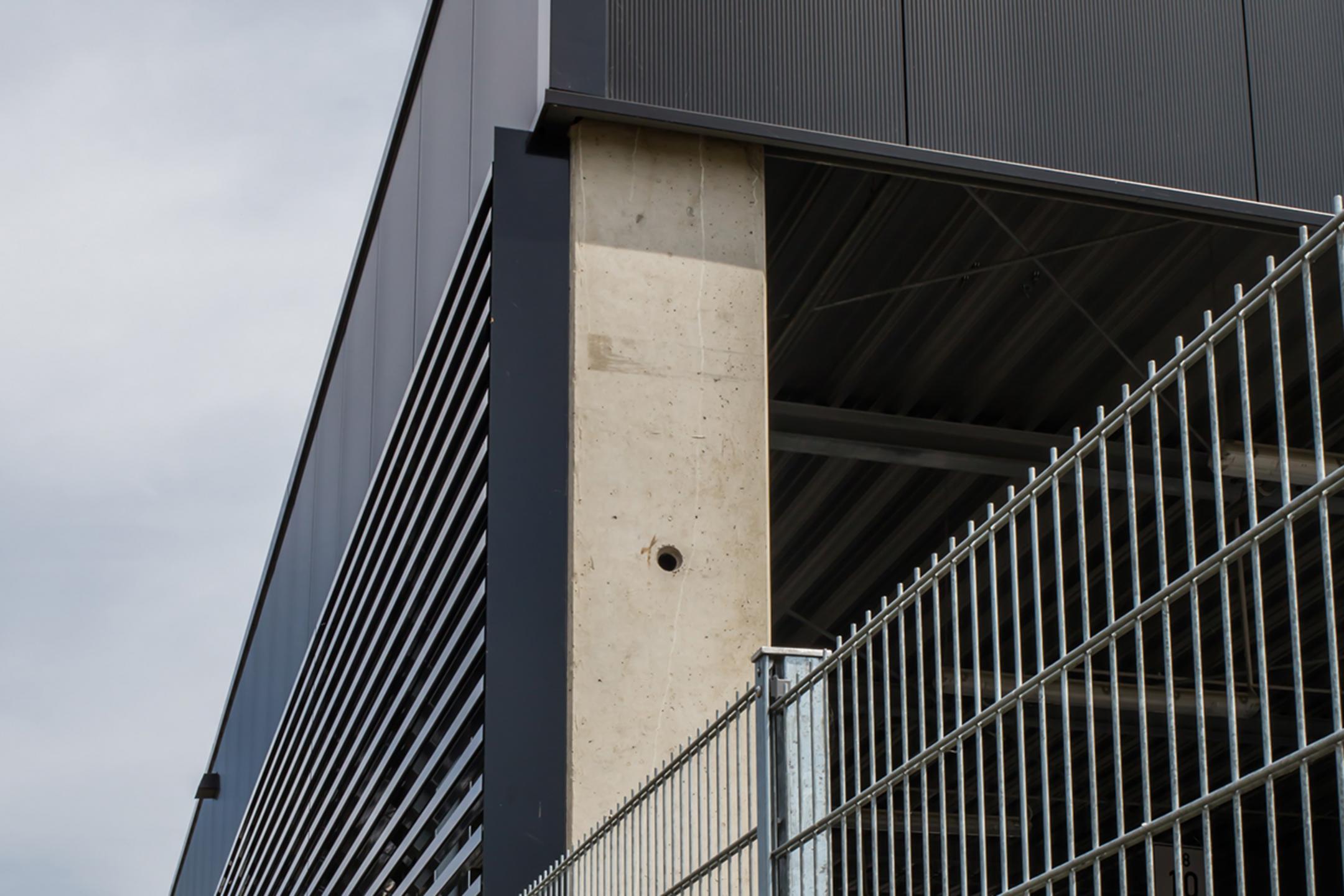 Der Firmenneubau aus der Nähe betrachtet, im Vordergrund ein Gitterzaun aus Metall.