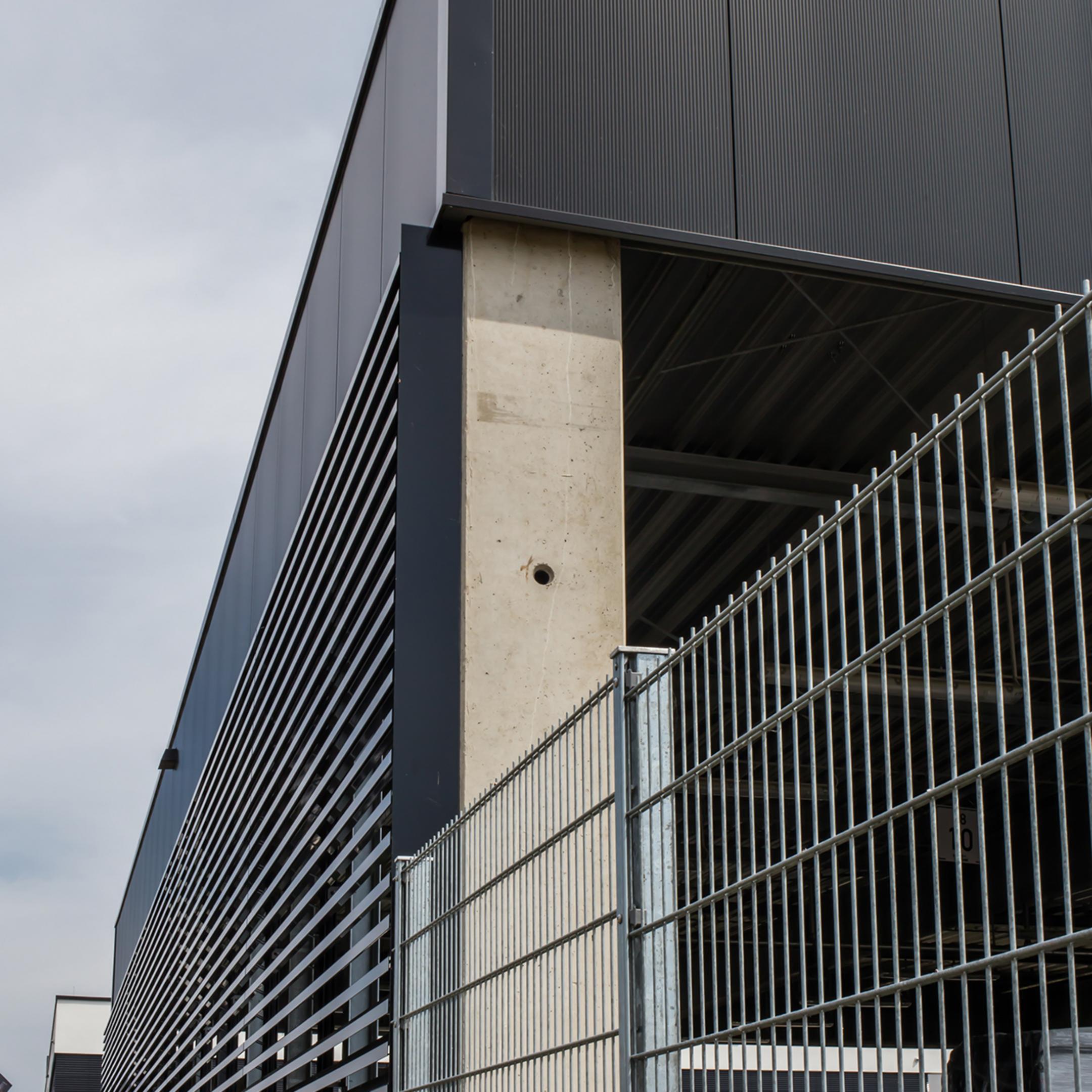 Der Firmenneubau aus der Nähe betrachtet, im Vordergrund ein Gitterzaun aus Metall.