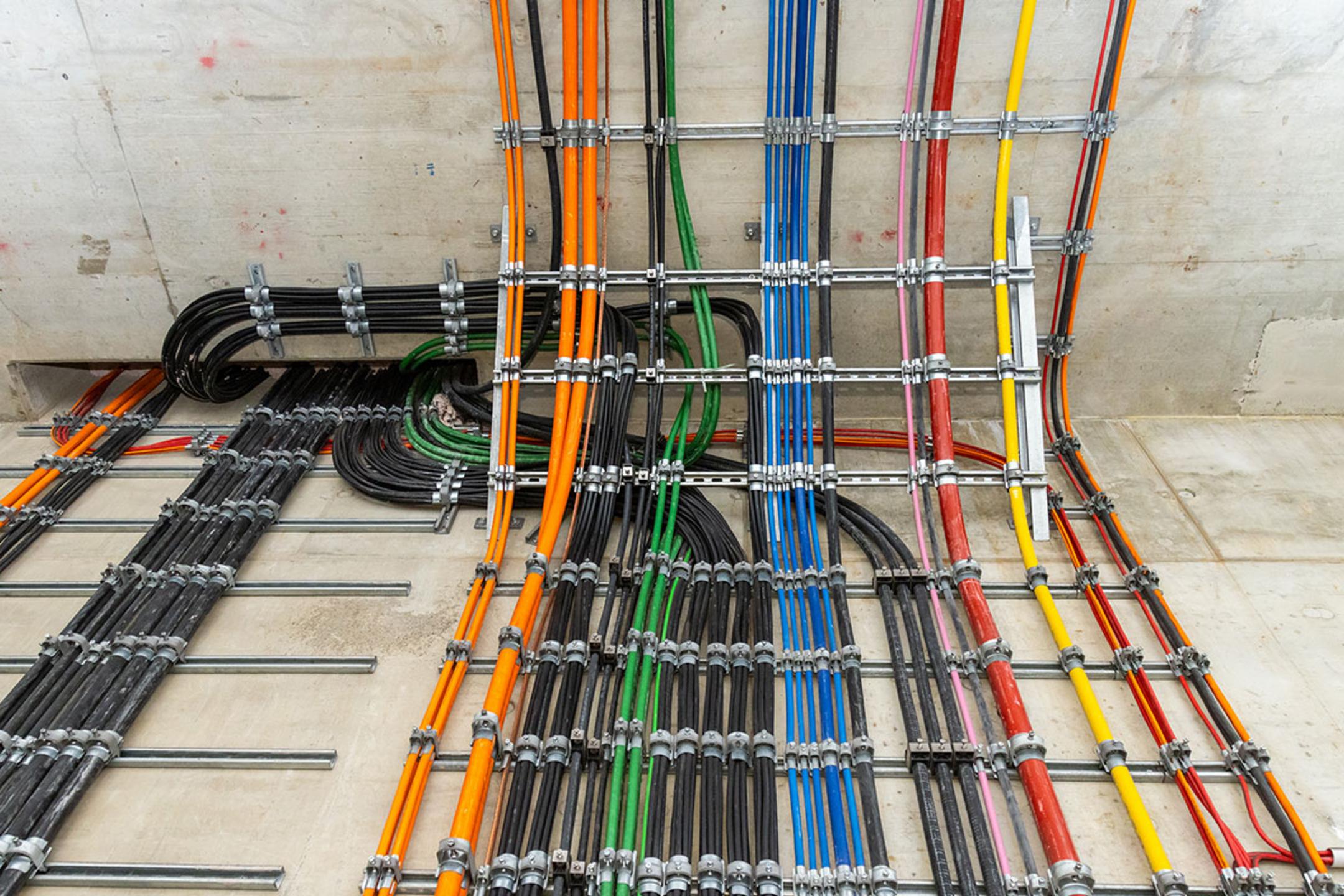 Farbcodierte Kabel verlaufen geordnet an der Wand entlang einer Tunneldecke