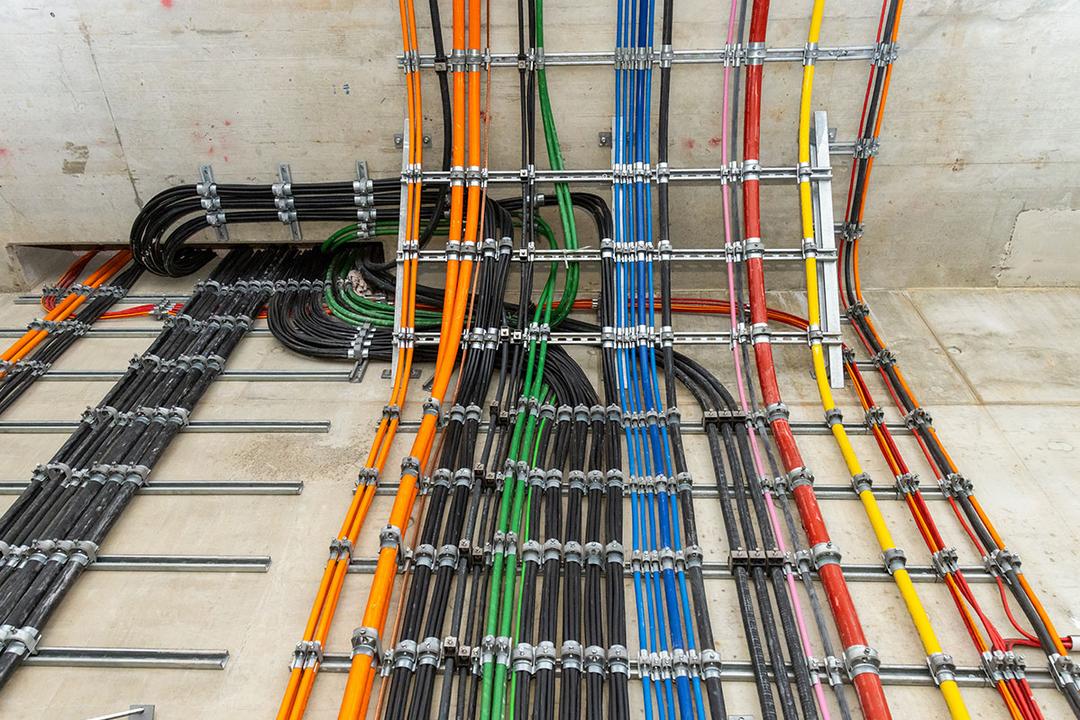 Farbcodierte Kabel verlaufen geordnet an der Wand entlang einer Tunneldecke