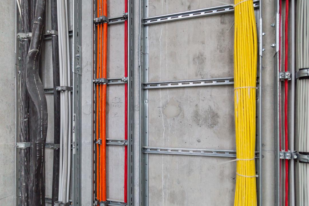 Saubere Elektroinstallation mit farbcodierten Kabeln in stabilen Metalltrassen an der Wand montiert.