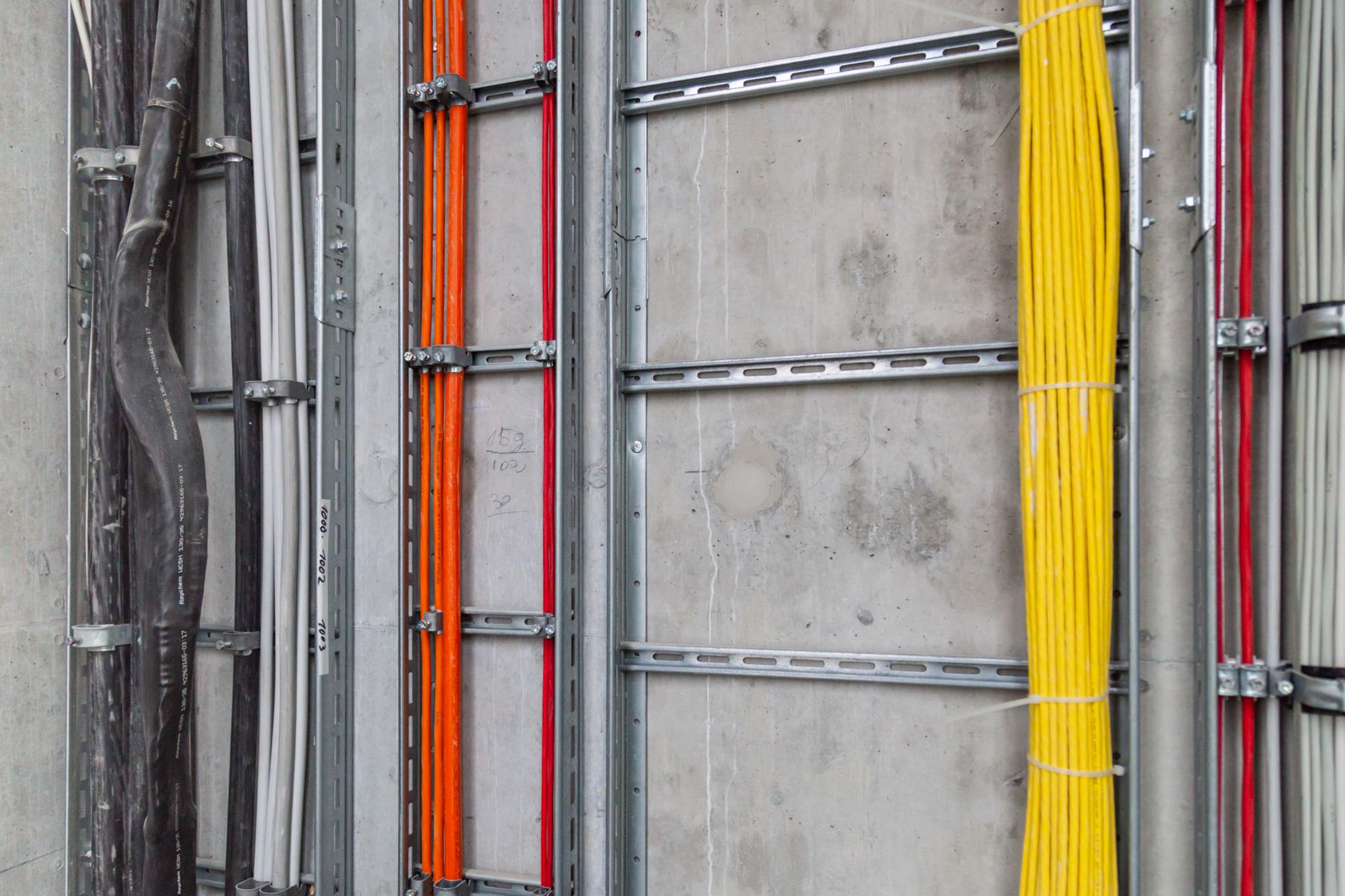 Saubere Elektroinstallation mit farbcodierten Kabeln in stabilen Metalltrassen an der Wand montiert.