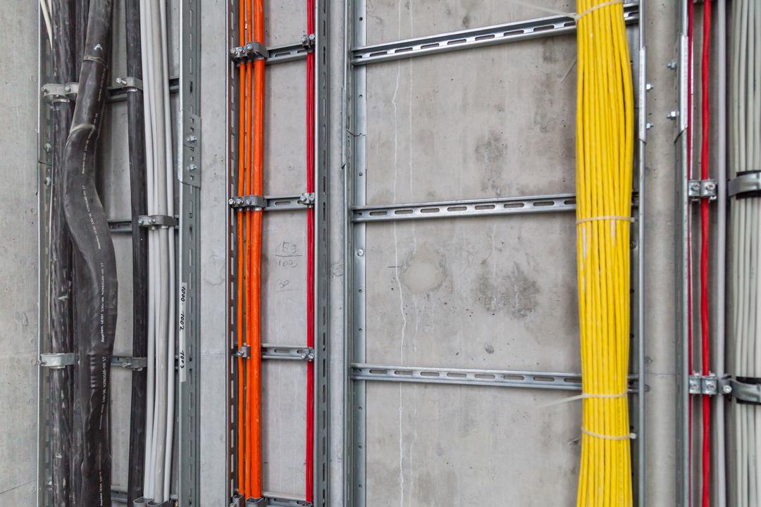 Saubere Elektroinstallation mit farbcodierten Kabeln in stabilen Metalltrassen an der Wand montiert.