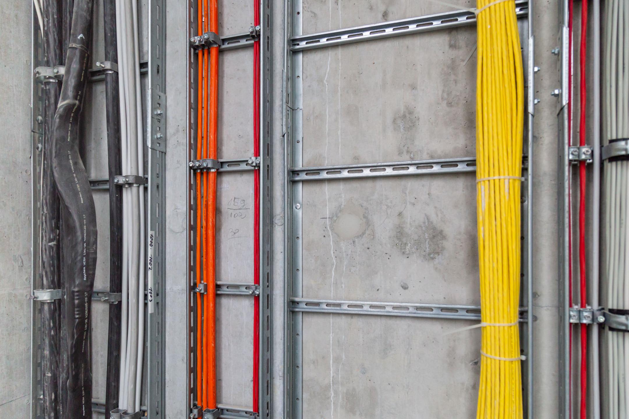 Saubere Elektroinstallation mit farbcodierten Kabeln in stabilen Metalltrassen an der Wand montiert.