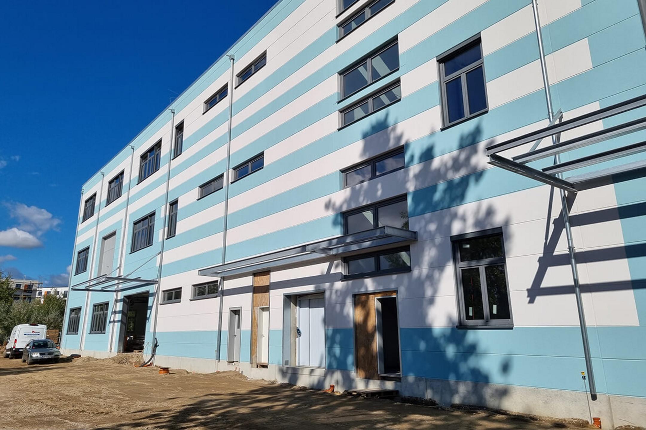 Der hellblau-weiß-gestreifte, moderne Erweiterungsbau von außen vor blauem Himmel.