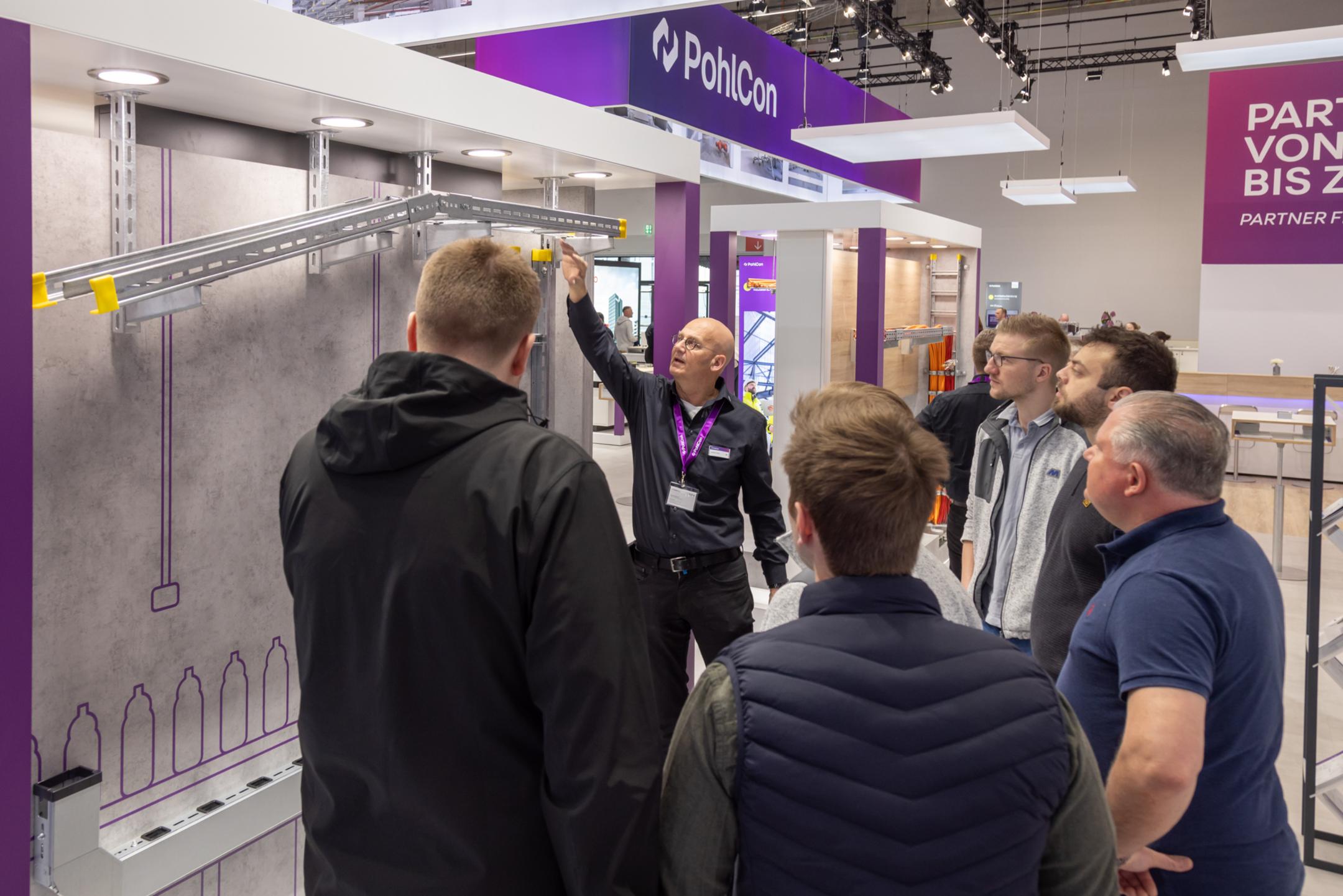Messestand mit dem Schriftzug PohlCon und mit Besuchern an einem Exponat