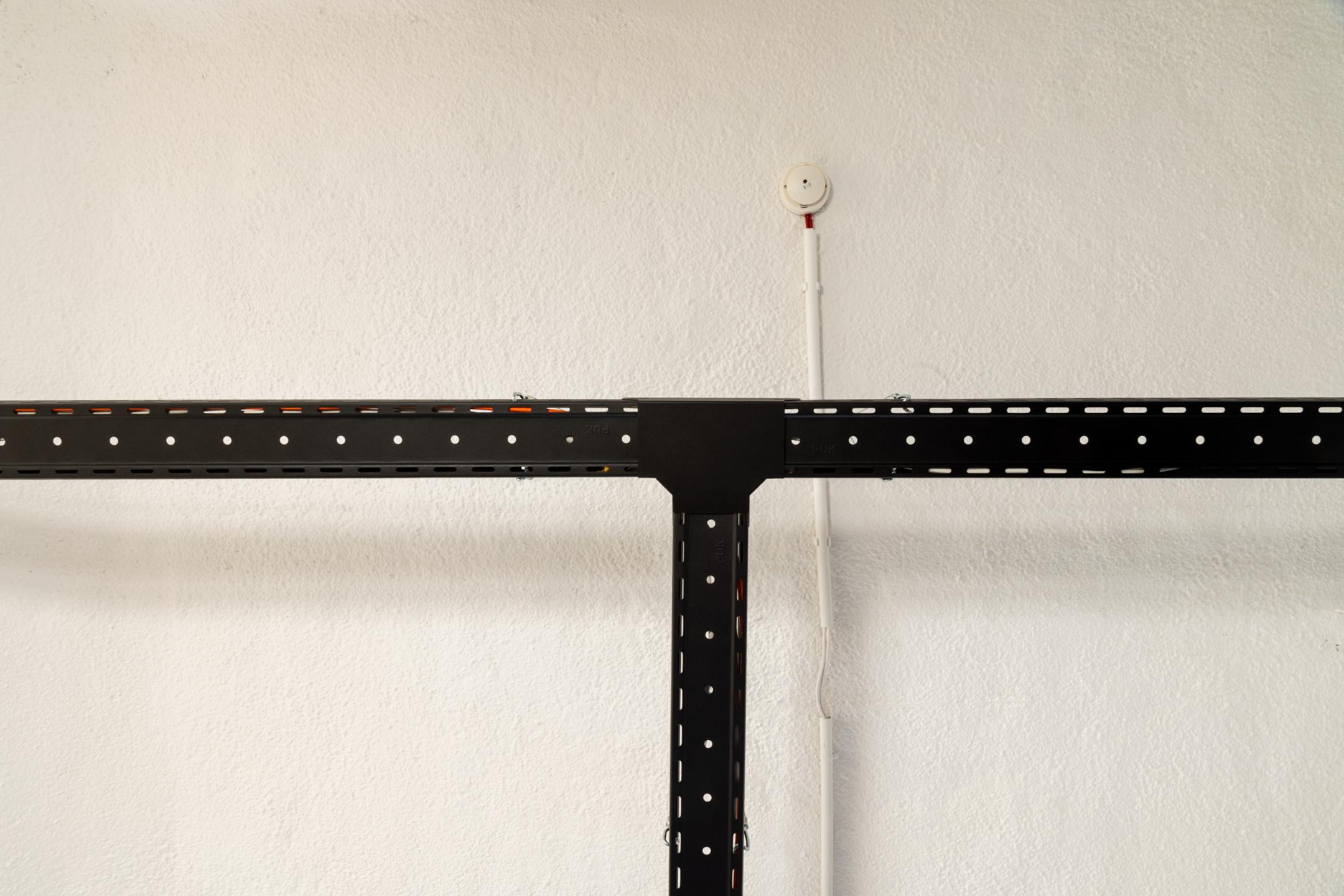 Detailansicht einer T-Kreuzung von schwarzen Kabelrinnen. die an der Decke abgehängt sind.