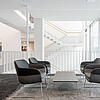 Moderne Lounge mit vier schwarzen Sesseln um einen Tisch, helle Treppe und große Fenster im Hintergrund