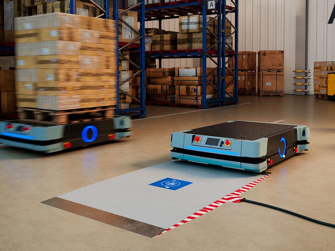 Blick in eine Lagerhalle, in der es ein Wireless Charging Protection System (WCPS) gibt, eine Infrastruktur für induktives Laden, die in den Boden eingelassen ist.