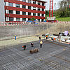 Bauarbeiter arbeiten an einem großen Baustellenfundament mit Glasfaserkunststoffarmierung in einer Baugrube vor einem roten Gebäude