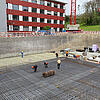Bauarbeiter arbeiten an einem großen Baustellenfundament mit Glasfaserkunststoffarmierung in einer Baugrube vor einem roten Gebäude