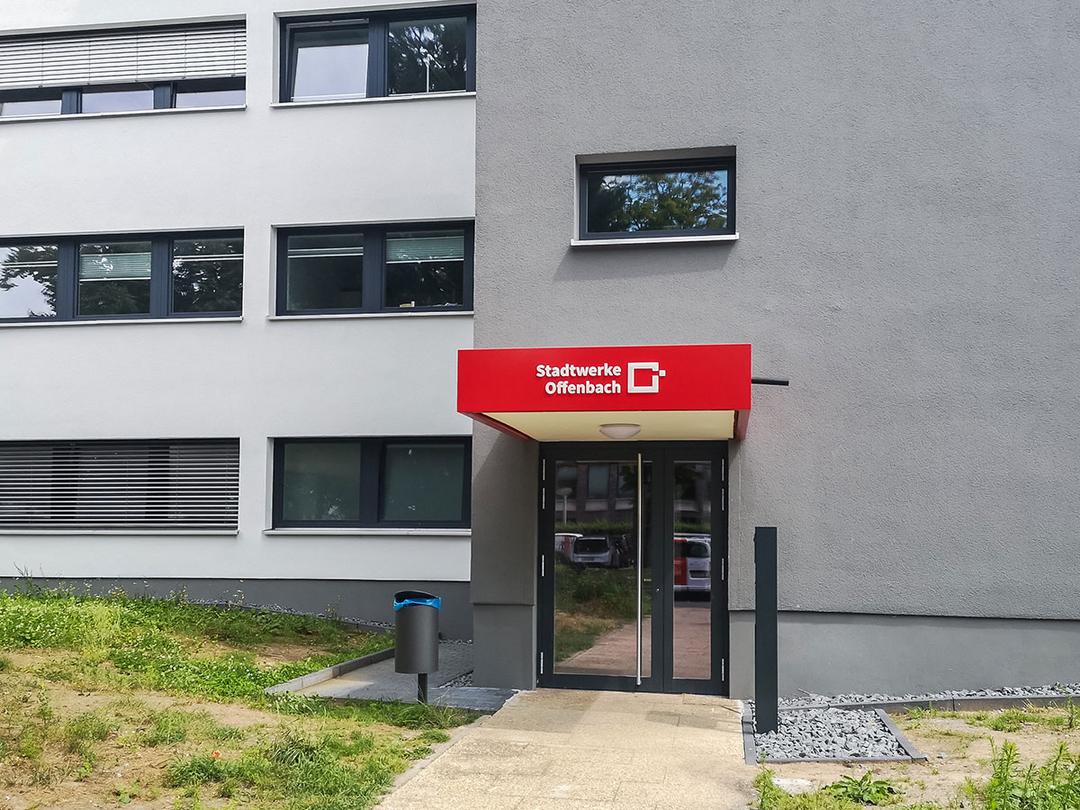 Eingang eines Gebäudes mit Vordach und Aufschrift 'Stadtwerke Offenbach' neben einer kleinen Rasenfläche