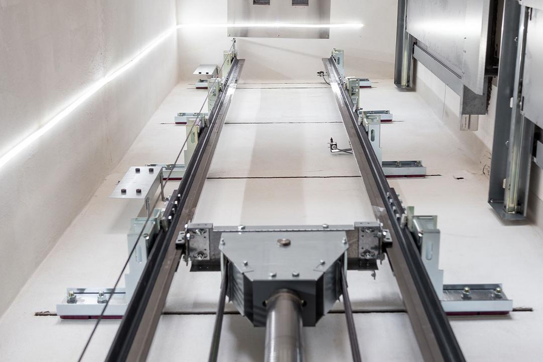 Blick in einen modernen Aufzugsschacht mit sichtbaren Führungsschienen, Seilen und LED-Beleuchtung an den Wänden