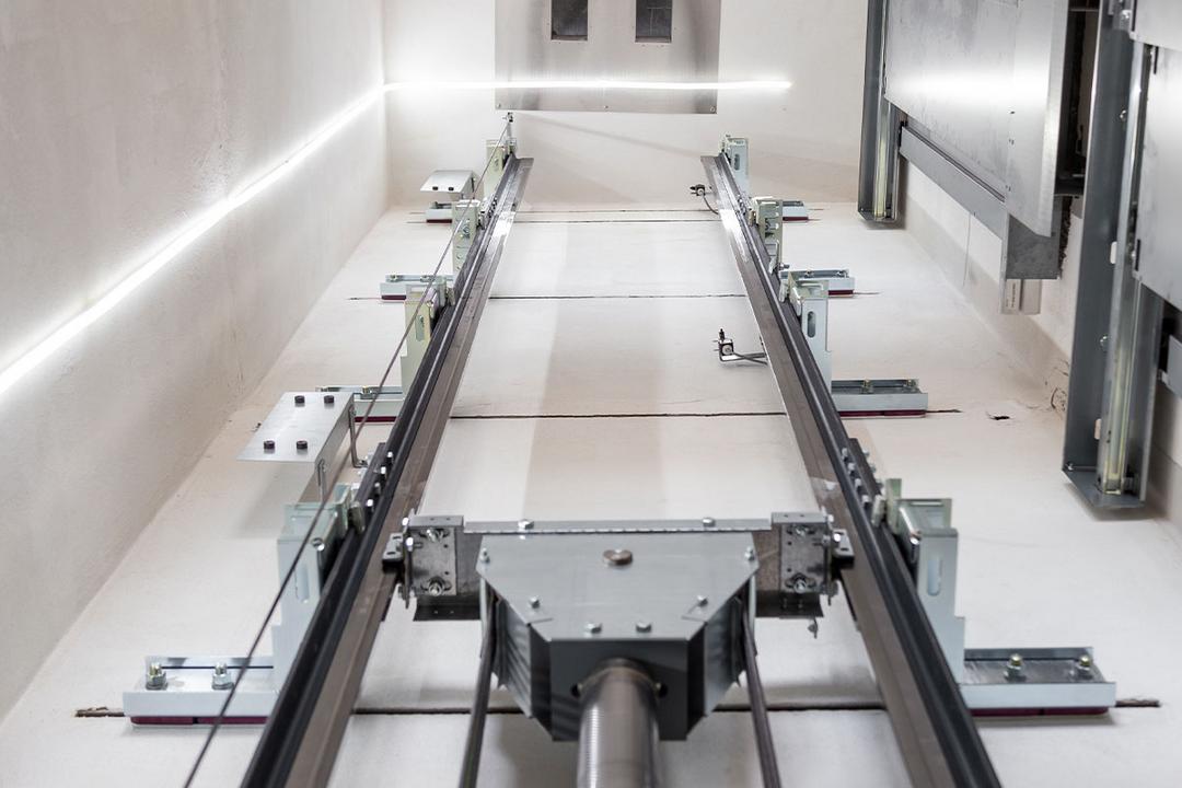 Blick in einen modernen Aufzugsschacht mit sichtbaren Führungsschienen, Seilen und LED-Beleuchtung an den Wänden