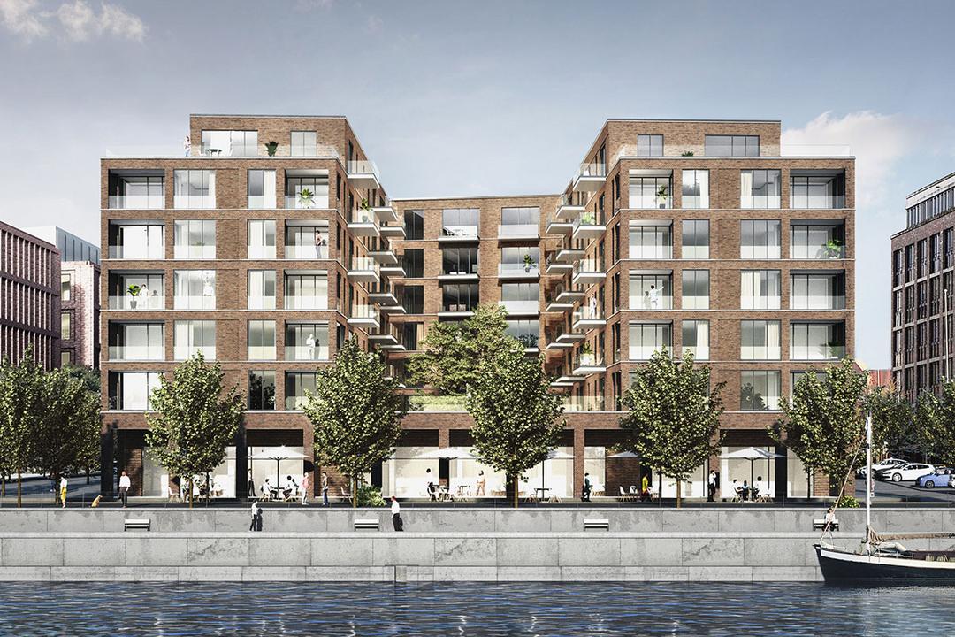 Modernes, mehrstöckiges Wohn- und Geschäftsgebäude aus Backstein an Uferpromenade mit Bäumen, Menschen und einem Segelboot im Wasser